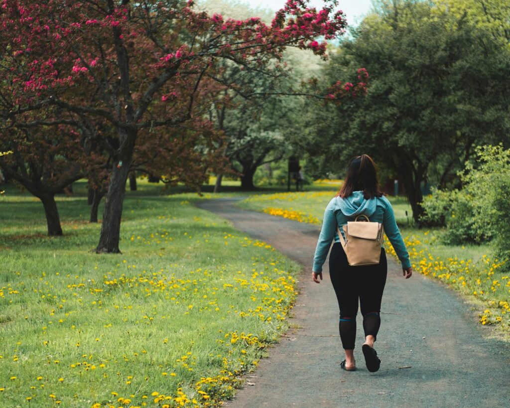 woman wearing blue jacket and black pants walking on grass field pathway