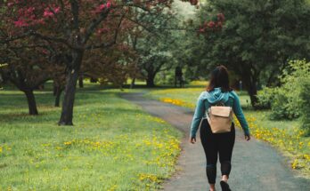 woman wearing blue jacket and black pants walking on grass field pathway