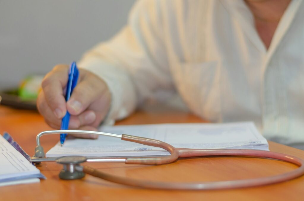 Clinician writing notes beside a stethoscope
