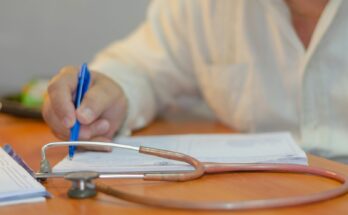Clinician writing notes beside a stethoscope