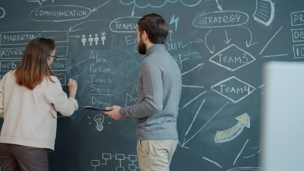 Colleagues reviewing diagrams on a chalkboard